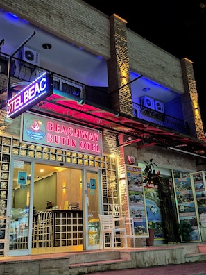 A hotel with a sign reading 'BEACHWAY BUTIK HOTEL' and a neon sign above it.