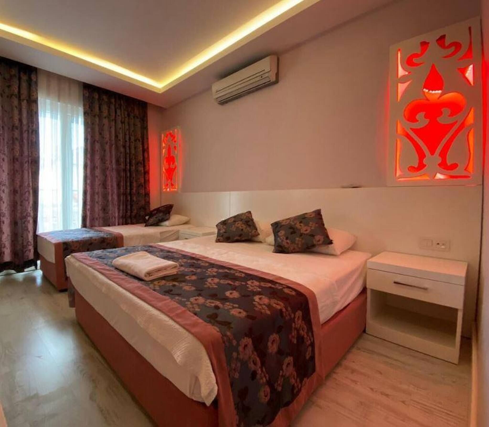 Une chambre d’hôtel avec un lit double, deux tables de chevet, une petite table d’appoint, un appareil de climatisation et un élément décoratif mural.