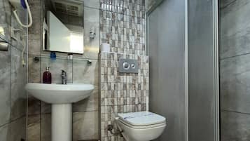 A bathroom with a pedestal sink, a toilet, a shower area, and a tiled wall.