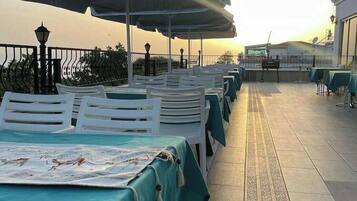 An outdoor dining area with tables and chairs, covered by umbrellas, and a tiled floor.