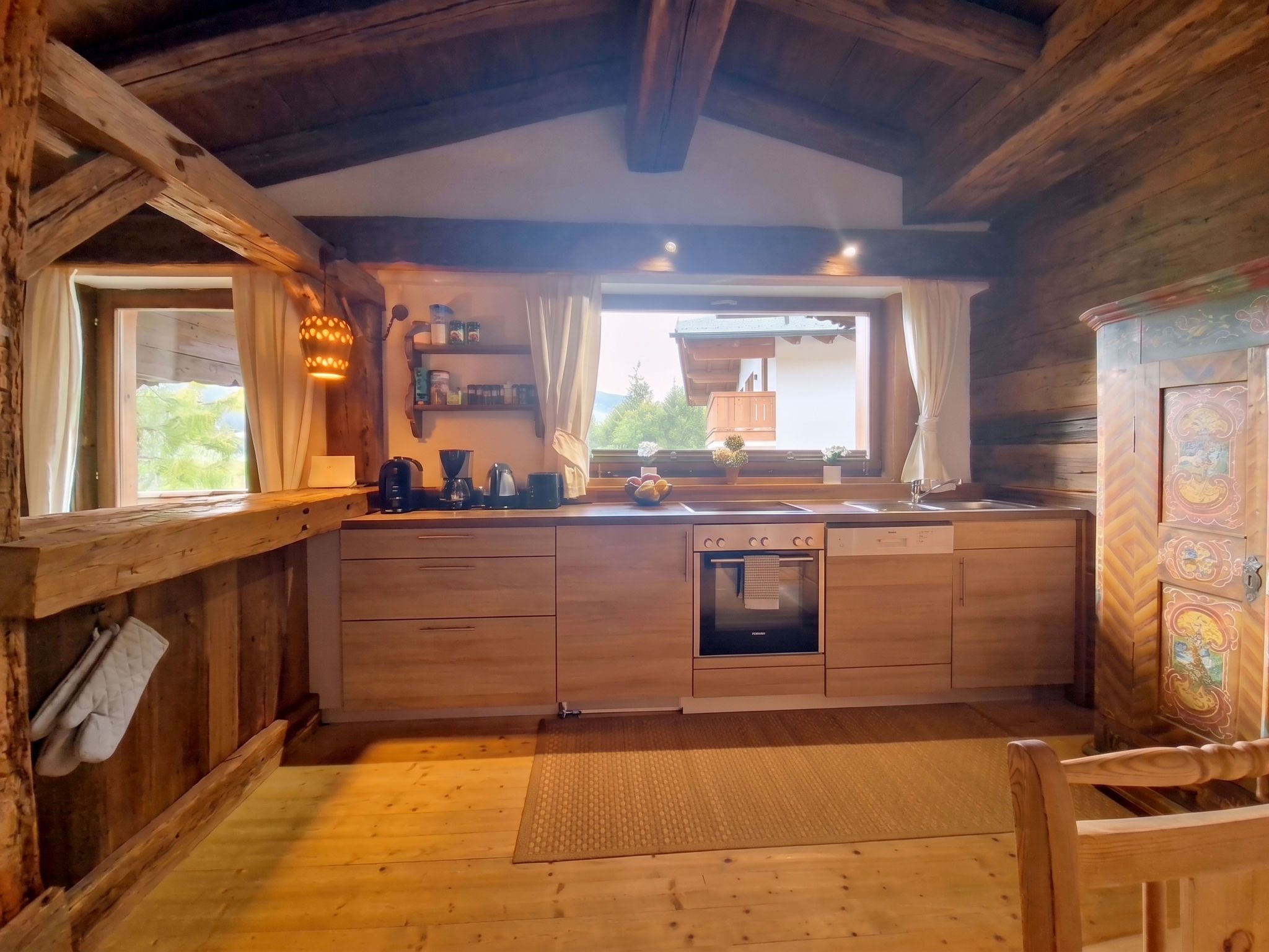 Une cuisine rustique aménagée dans une cabane en bois, avec un four encastré, un évier et une fenêtre donnant sur la verdure.