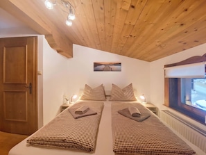 A bedroom with two beds, wooden ceiling, a painting, bedside lamps, and a window. - Manharthof by Interhome (Kirchberg in Tirol)