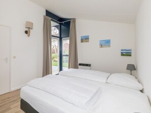 A bedroom with a bed, a window with curtains, a wall-mounted lamp, and a small picture on the wall. - Holiday Home in Renesse With Swimming Pool (Renesse)