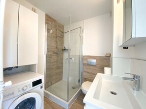 A modern bathroom with a glass-enclosed shower, a built-in washing machine, and a sink with a mirror. - Apartment in Westkapelle With Wi-fi (Westkapelle)