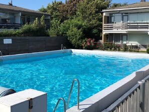 A clear blue swimming pool with a wooden deck and metal handrails. - Apartment in Westkapelle With Wi-fi (Westkapelle)