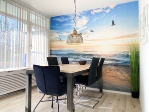 A dining area with a mural of a beach scene, a hanging light fixture, and a potted plant. - Apartment in Westkapelle With Wi-fi (Westkapelle)