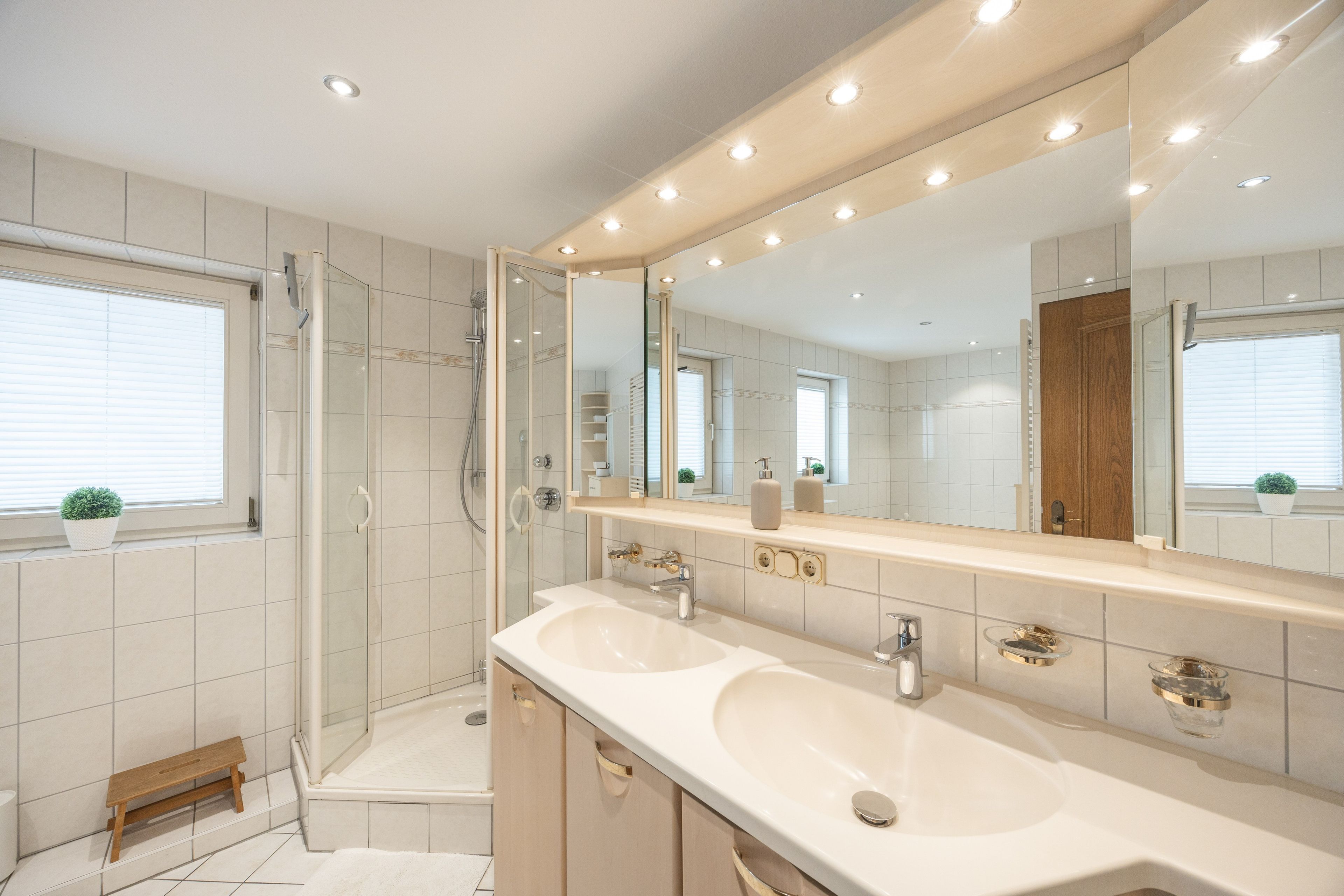Ein modernes Badezimmer mit barrierefreier Dusche, einem Doppelwaschbecken und einem großen Spiegel.