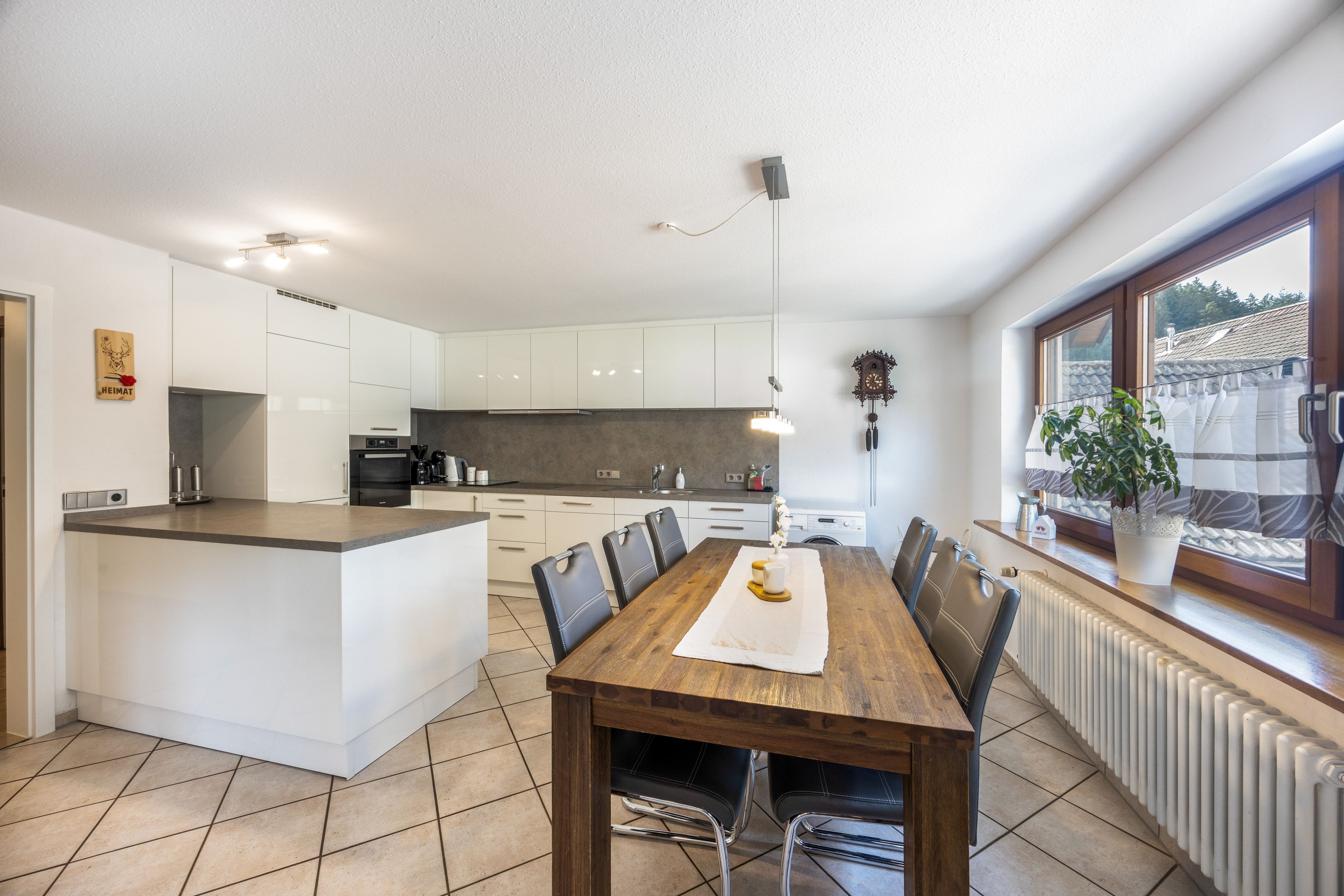 A modern kitchen with white cabinetry, a central island, and a dining area with a wooden table and chairs.