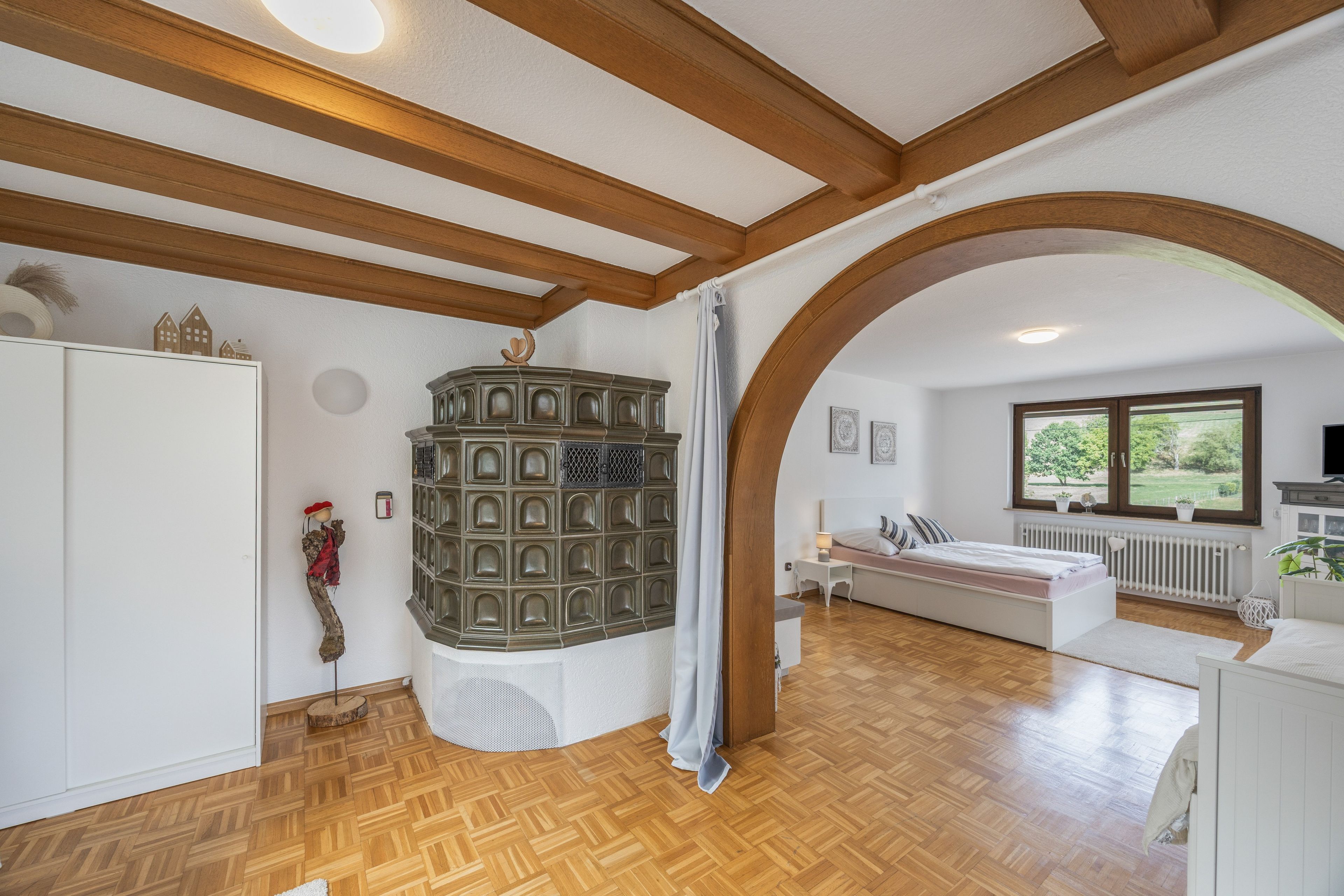 A bedroom with a wooden floor, a bed, a window, and a white wardrobe.