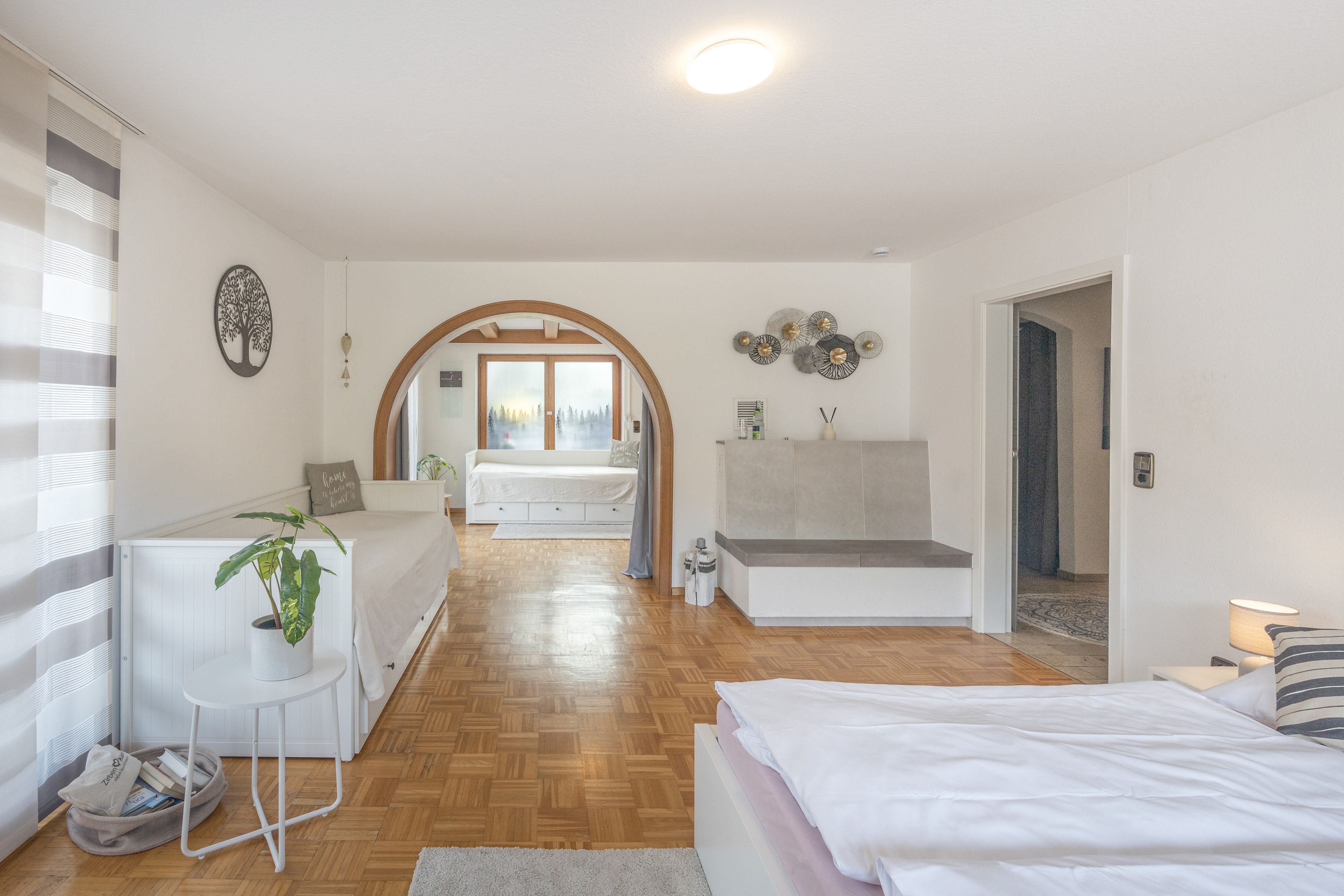 Ein modernes Schlafzimmer mit Holzboden, einem Bett, einer Couch und einem Schreibtisch.