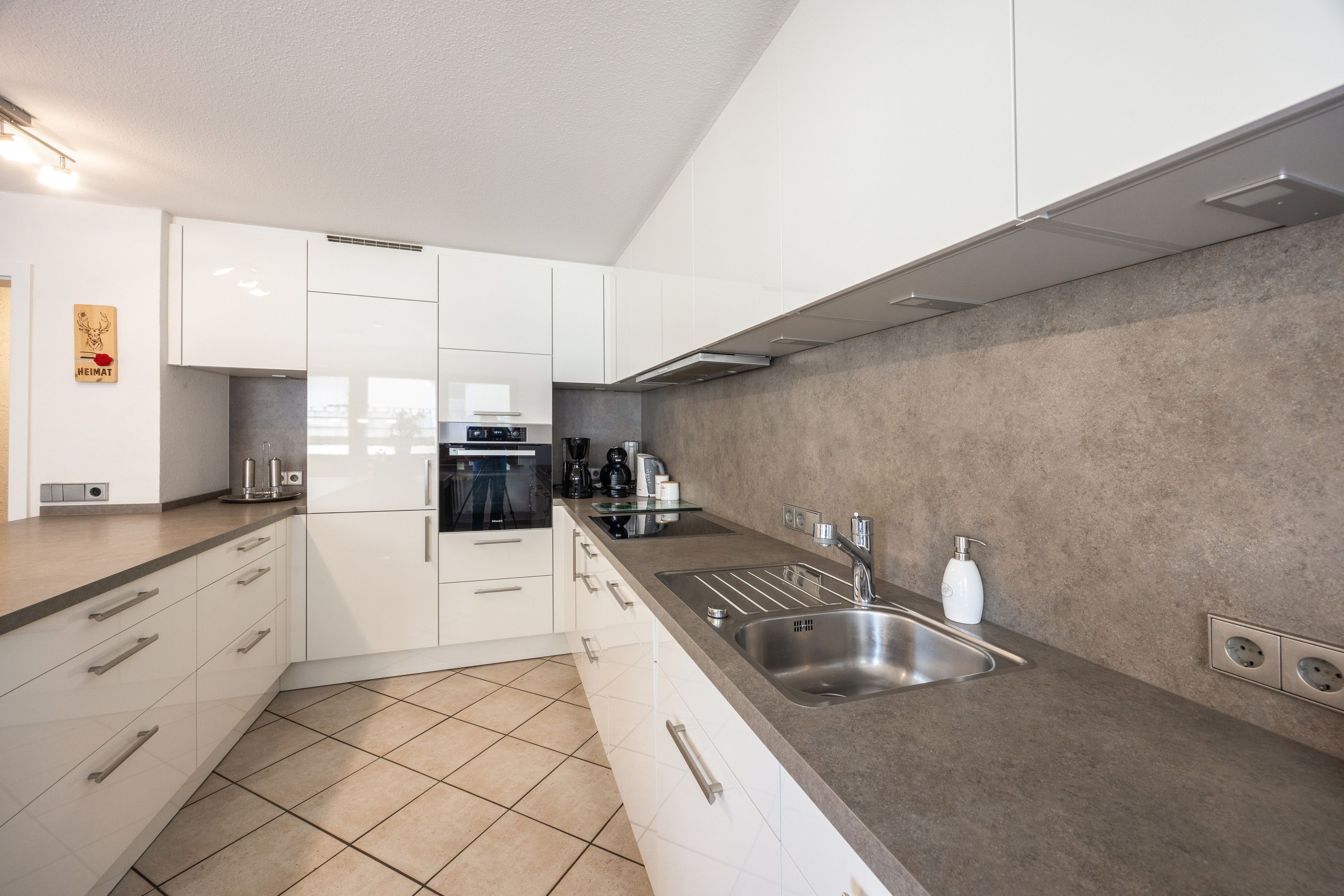 A modern kitchen with white cabinets, a stainless steel sink, and a grey countertop.