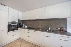 A modern kitchen with white cabinets, a stainless steel sink, and a built-in oven.