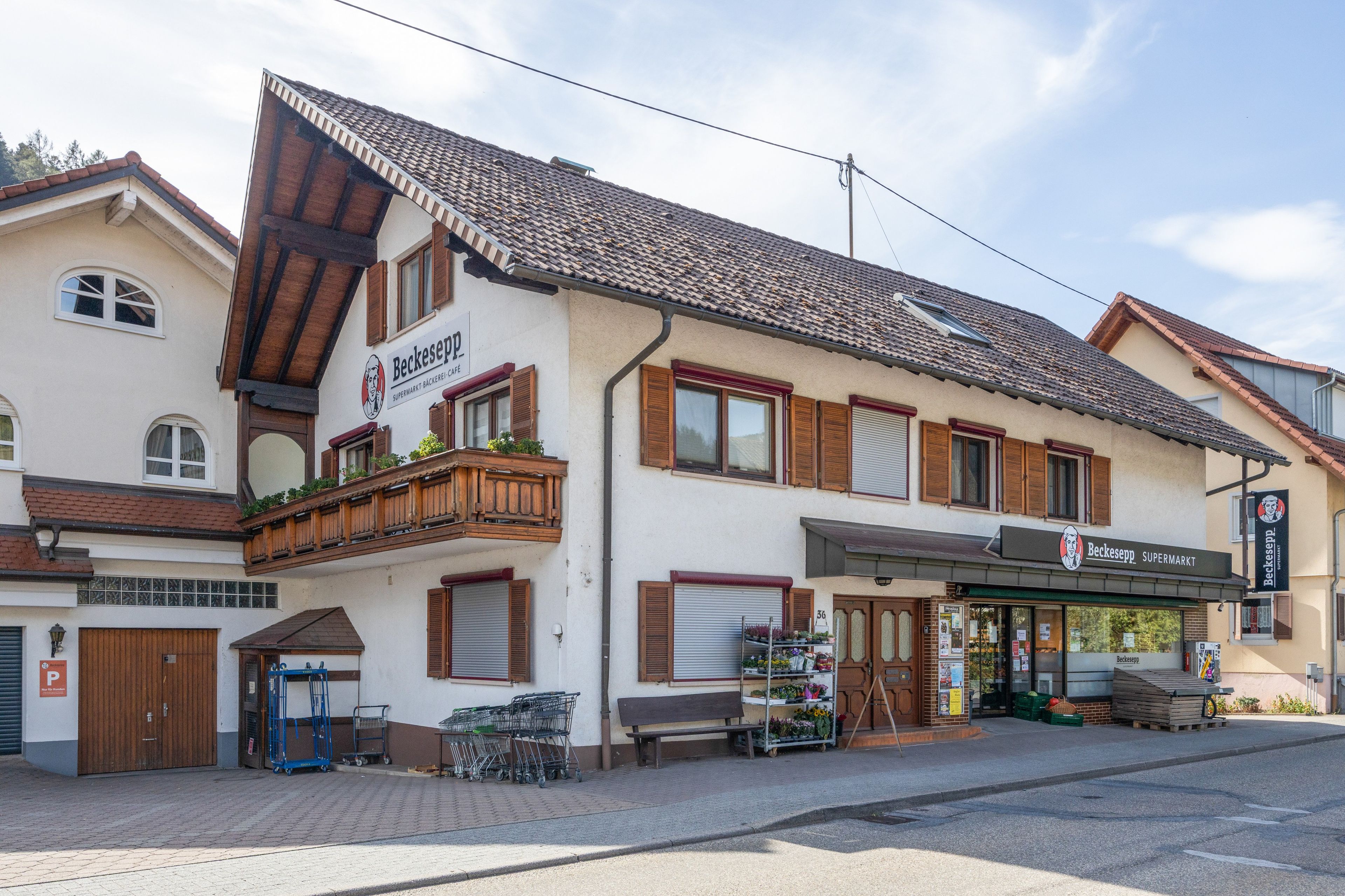 Ein zweistöckiges Gebäude mit einem Schild für 'Beckespp' im Erdgeschoss, einem Balkon mit Holellentrailungen und einer Reihe geschlossener Fensterläden im Obergeschoss.