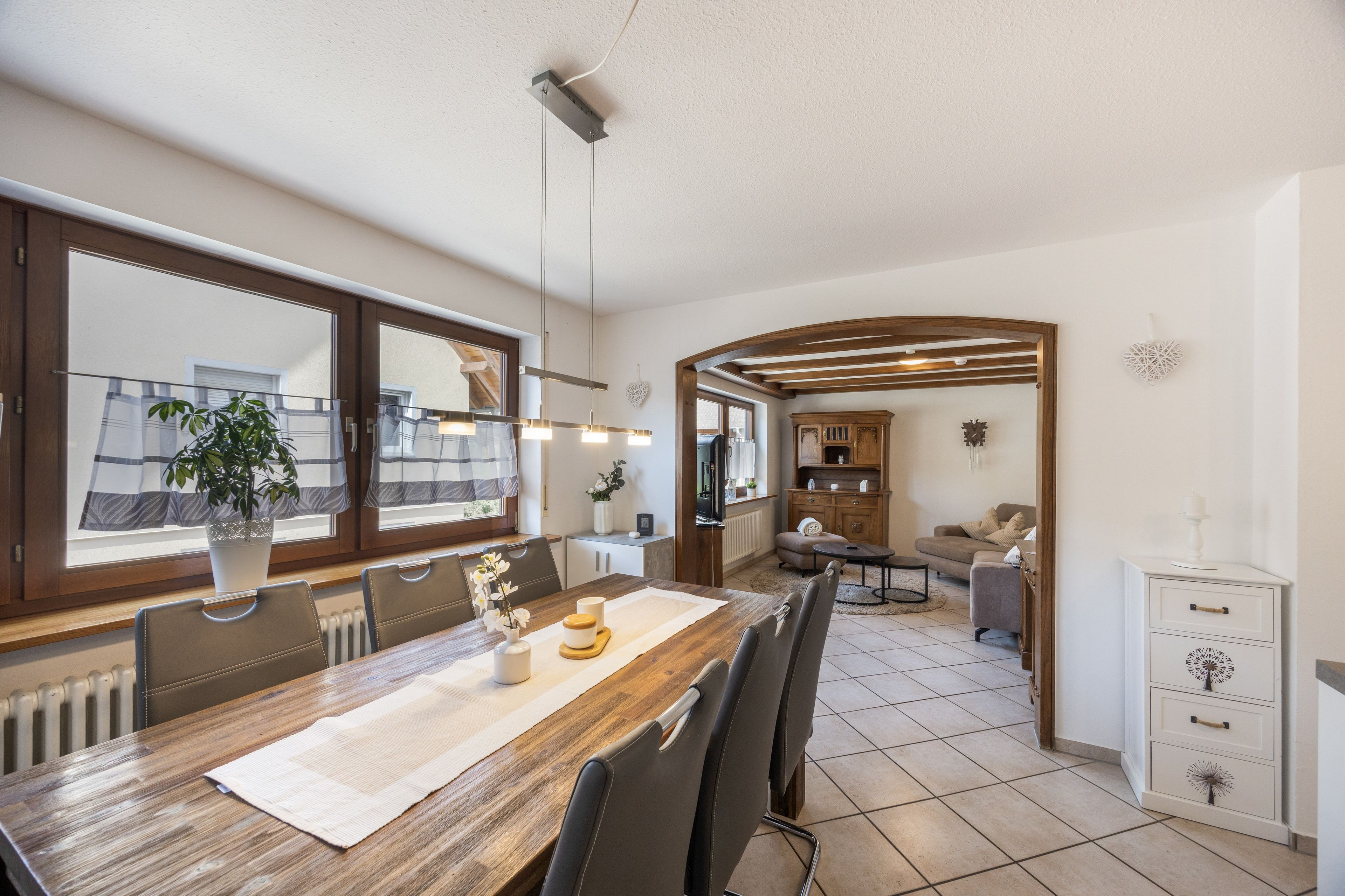 Ein Essbereich mit Holztisch, Stühlen und Blick auf die Küche und das Wohnzimmer durch einen Bogen.