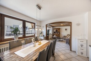A dining area with a wooden table, chairs, and a view of the kitchen and living room through an archway.