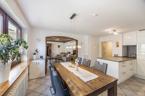 A modern kitchen with a wooden dining table, white cabinets, and a view to the living area. - Sommer Apartments Black Forest: Mountain View, Balcony & Wi-Fi – Family Friendly (Simonswald)
