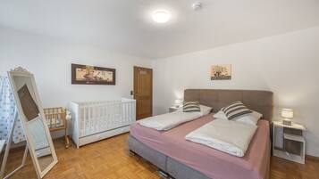 Ein Schlafzimmer mit einem Doppelbett, einem Babybett, Holzboden und einer Tür.