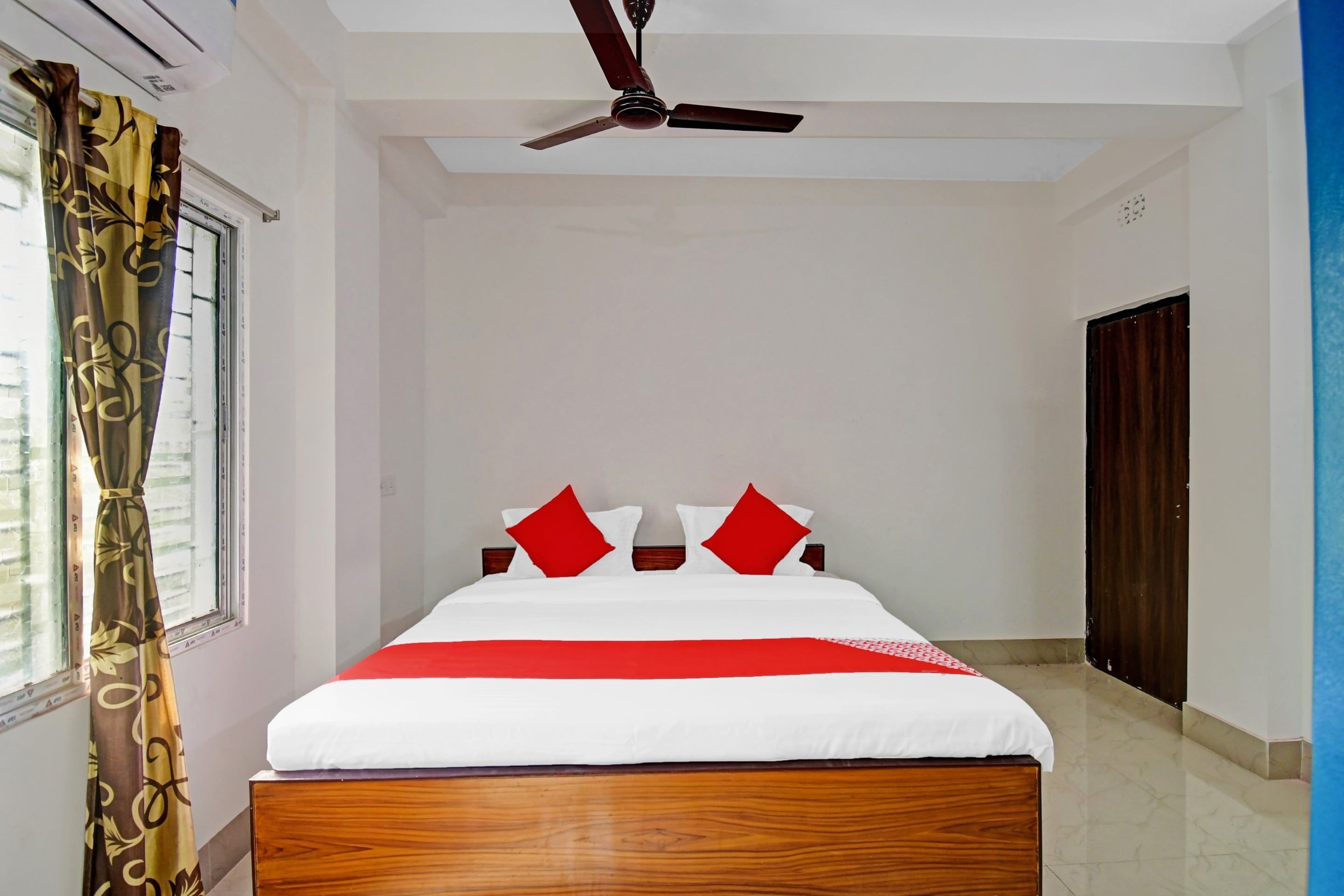 Una habitación de hotel con cama, ventilador de techo, ventana con cortinas y una puerta.