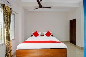 Una habitación de hotel con cama, ventilador de techo, ventana con cortinas y una puerta.