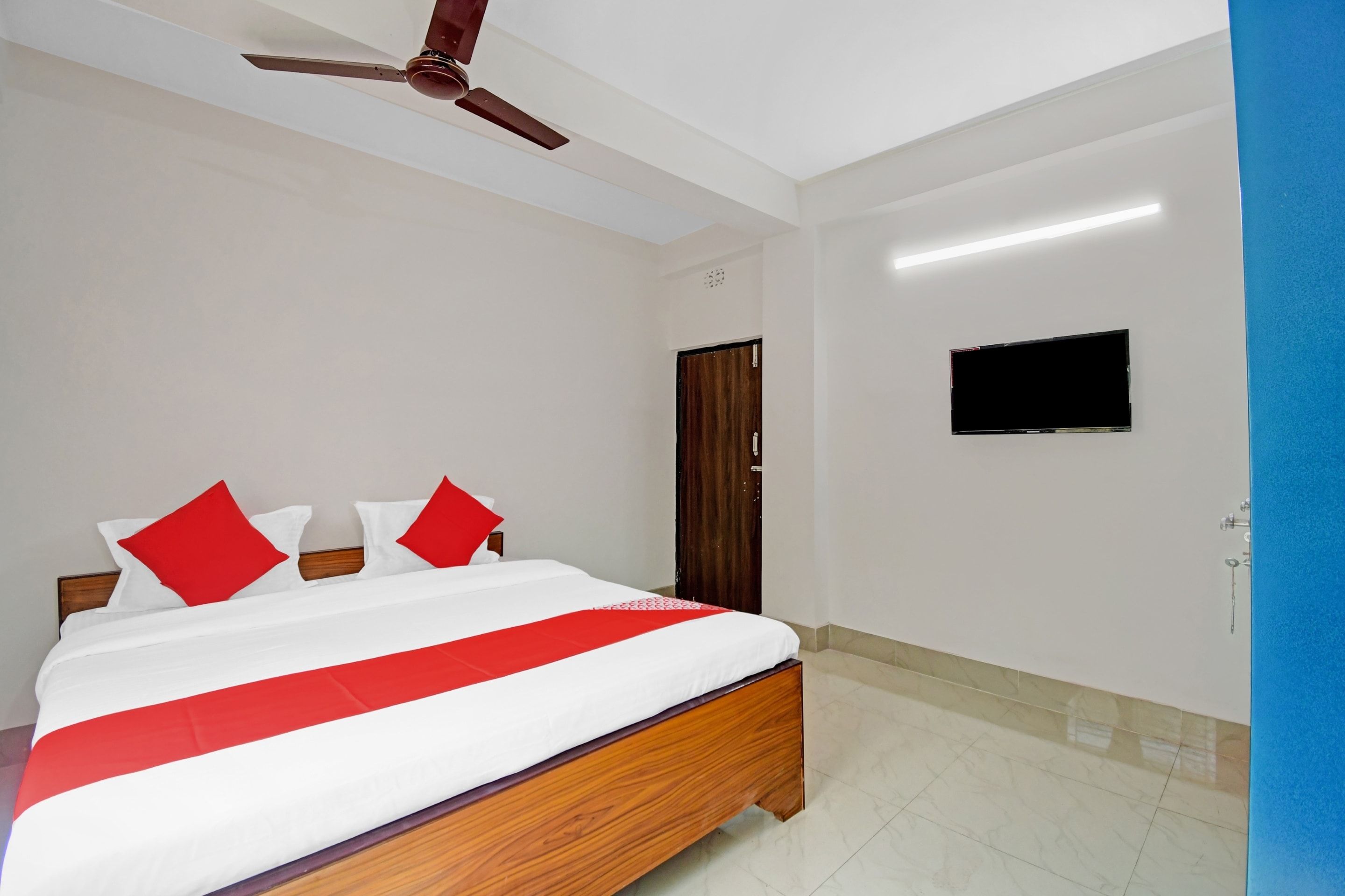 Un dormitorio con cama, ventilador de techo, televisor y una puerta.