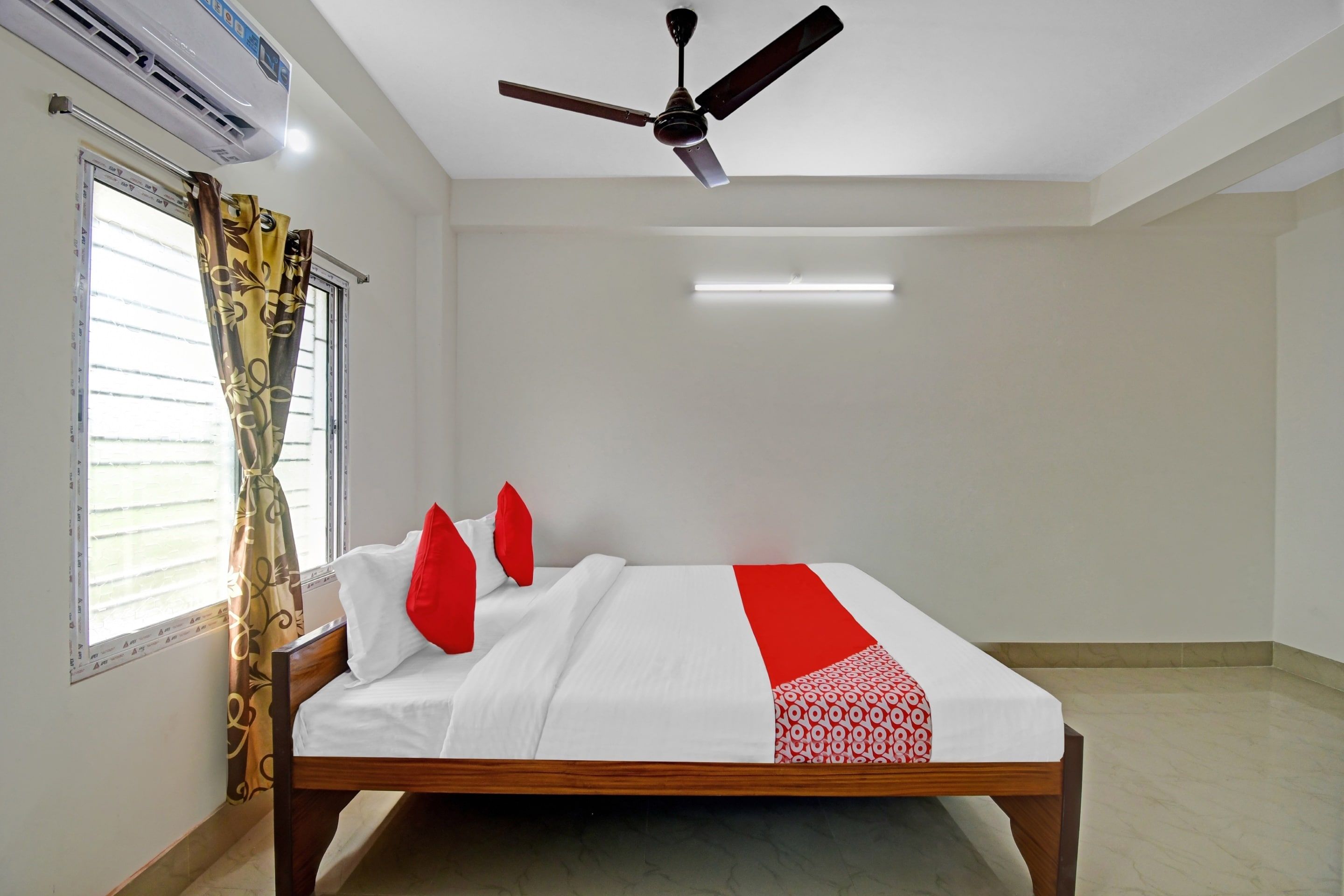 Una habitación de hotel con una cama, ventilador de techo, aire acondicionado y ventana con cortinas.