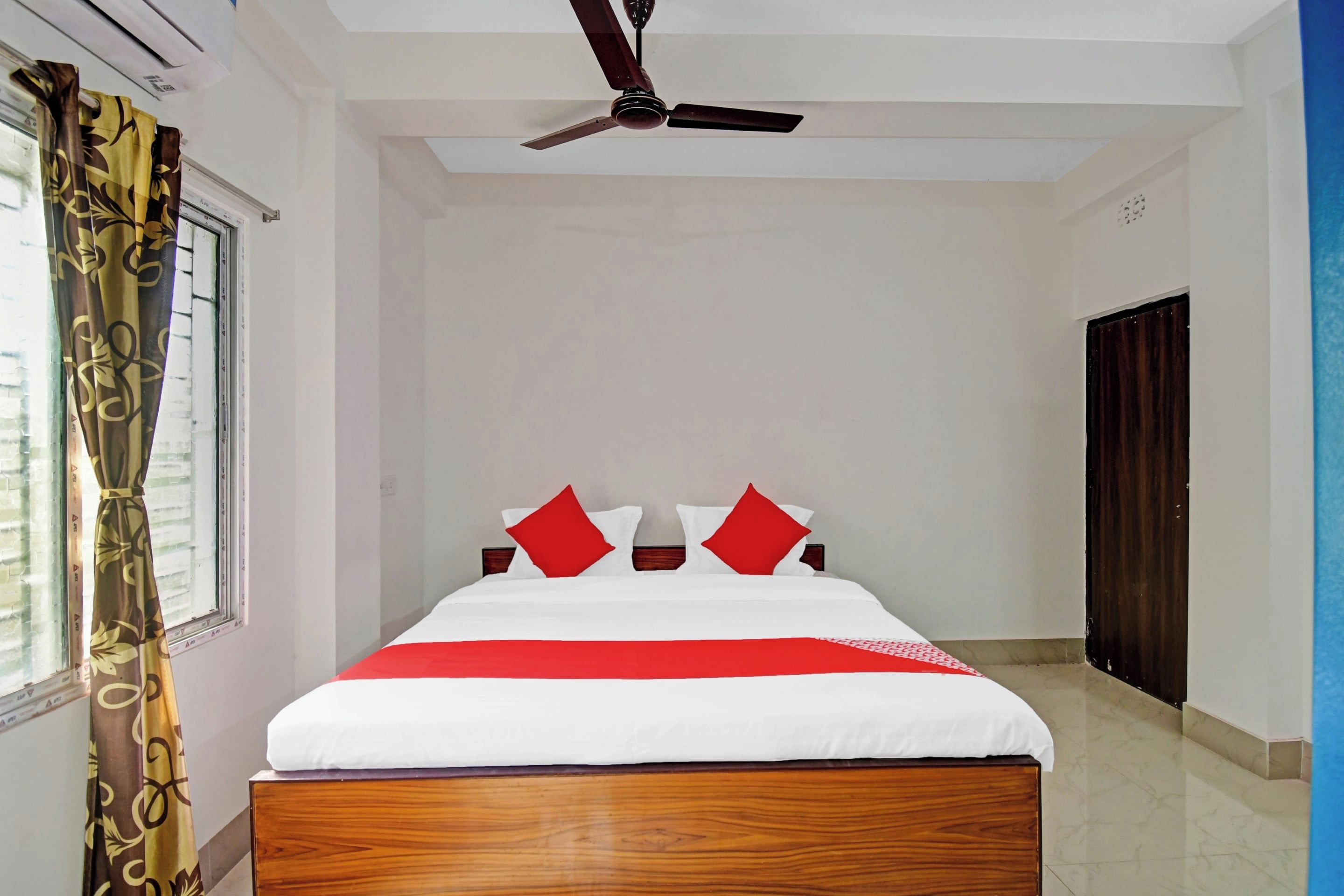 Habitación de hotel con una cama, ventilador de techo, ventana con cortinas y una puerta.