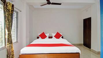 Habitación de hotel con una cama, ventilador de techo, ventana con cortinas y una puerta.