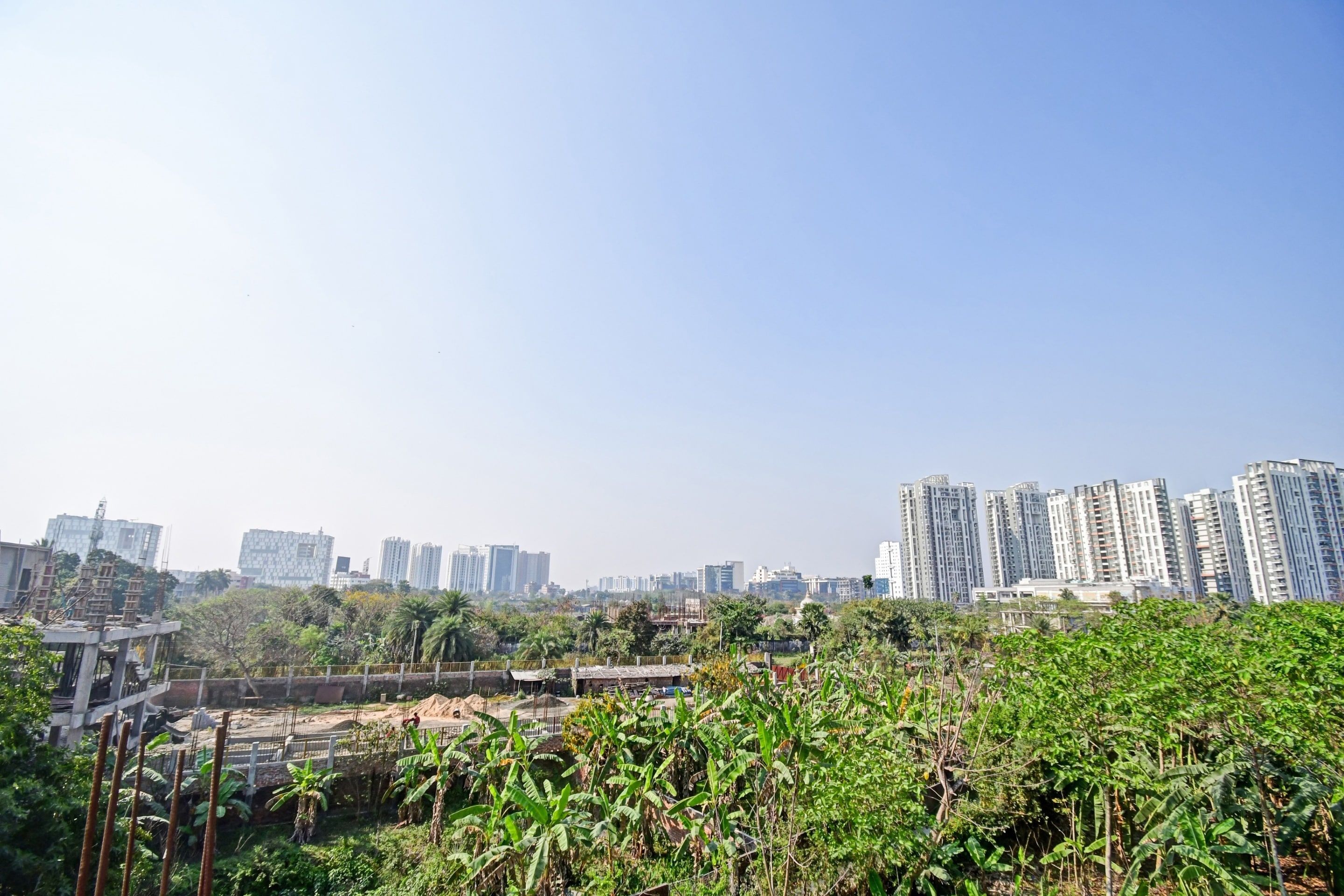 Un paisaje urbano con rascacielos, una obra en construcción y abundante vegetación.