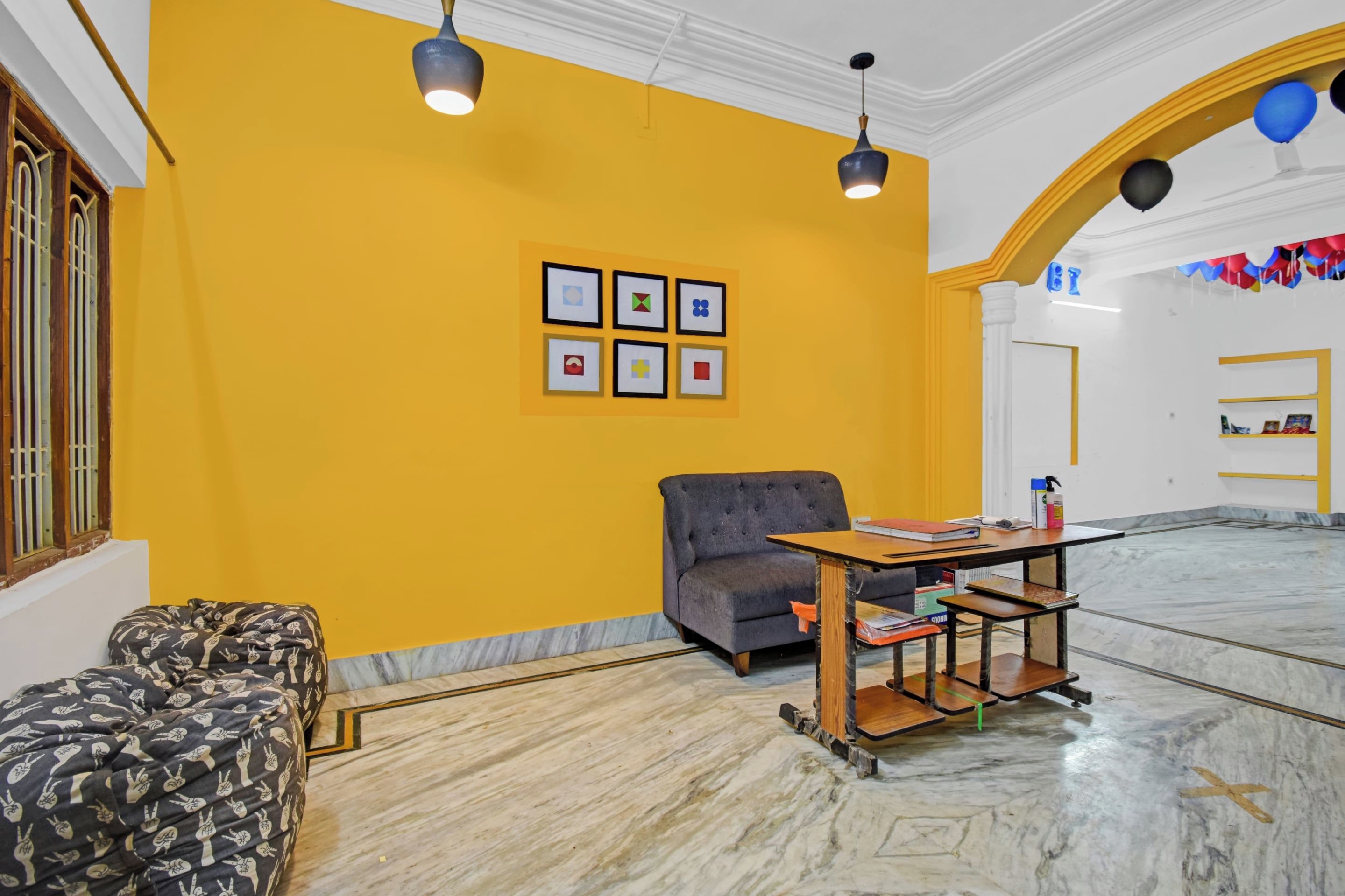 Una habitación con una pared amarilla, un sofá gris, una mesa de madera con objetos y cuadros enmarcados.