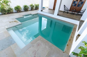 Ein Swimmingpool mit glatter, blauer Wasseroberfläche, umgeben von einer gefliesten Terrasse und Blumentöpfen.