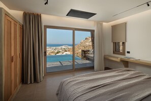 A bedroom with a large sliding glass door leading to a balcony with a view of a coastal landscape. - GkF - Luxury Panoramic Suite (Naxos)
