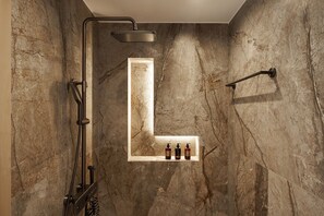 Ein Badezimmer mit Dusche, einer Marmorwand und einem Ablagebereich für Pflegeartikel.