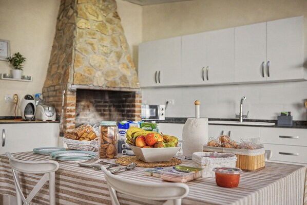A kitchen with a stone chimney, white cabinets, and a dining table set with plates, cutlery, and food items. - Room 'Mirador' with shared terrace, Wi-Fi and air conditioning (Poblenou del Delta)