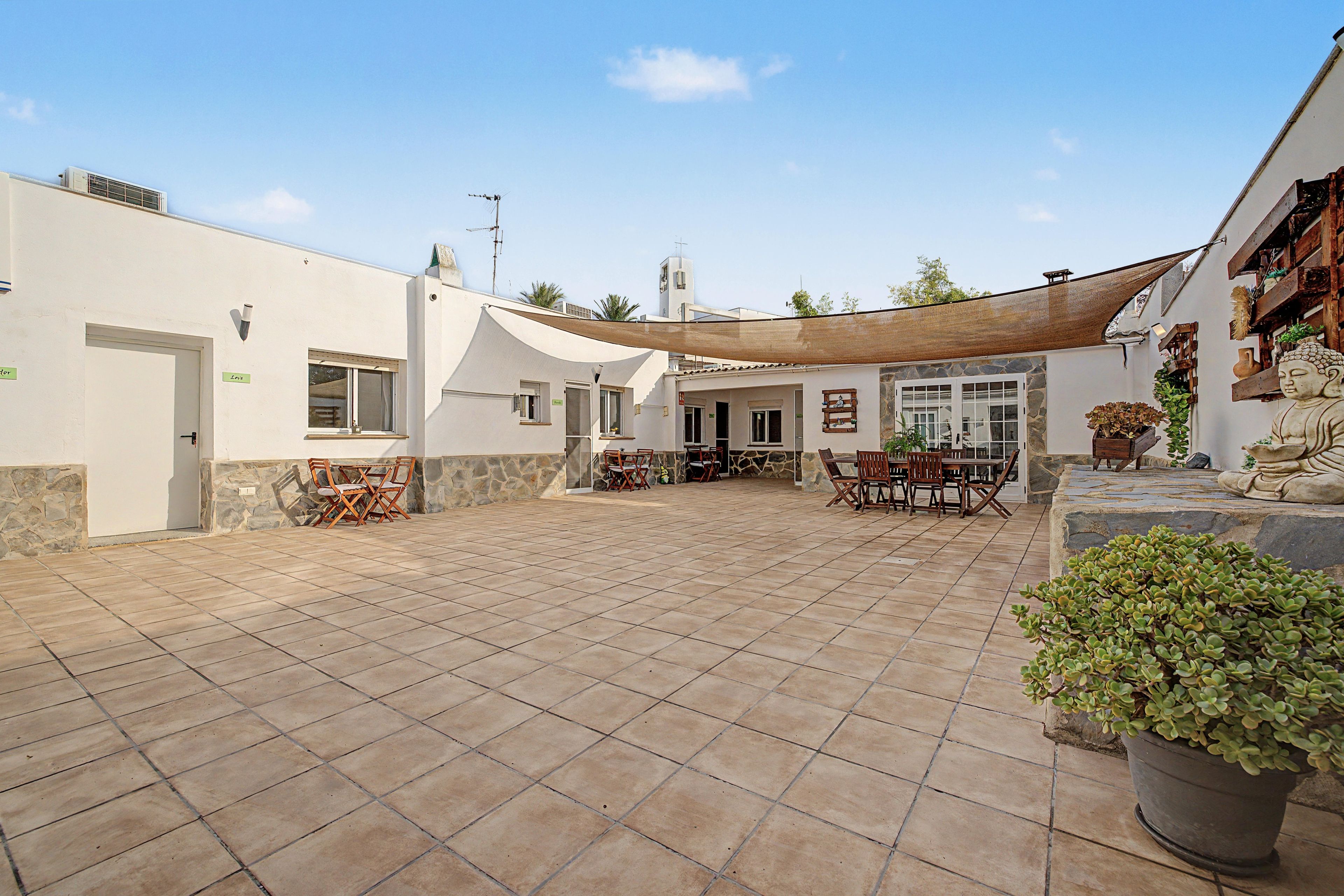 Un patio con suelo de baldosas, mobiliario exterior y una estatua de Buda.