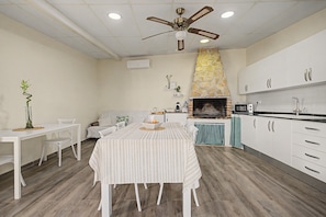 A modern kitchen with white cabinetry, a stone fireplace, and a dining area with a striped tablecloth. - Room 'Mirador' with shared terrace, Wi-Fi and air conditioning (Poblenou del Delta)