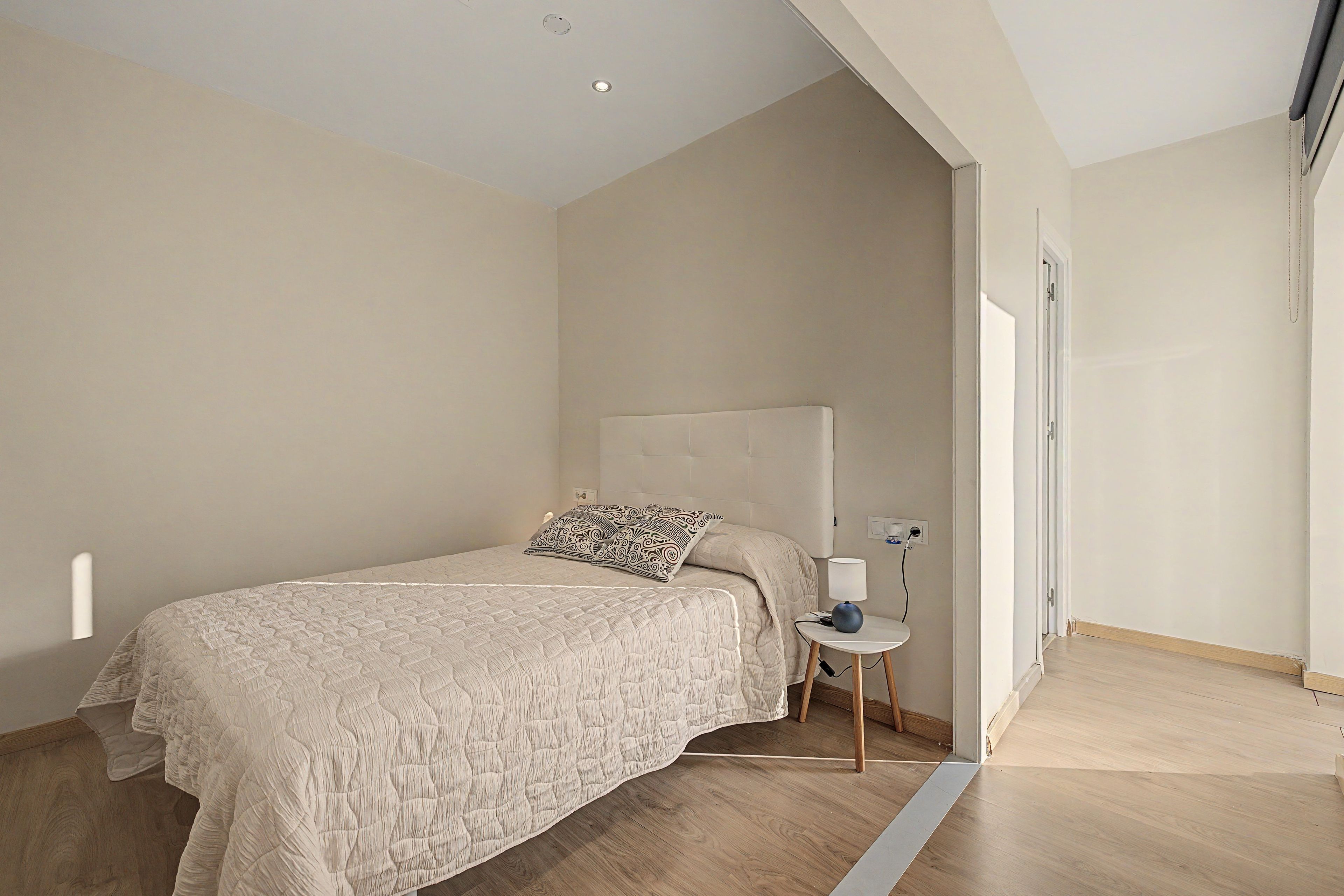 Un dormitorio con cama, mesita de noche, lámpara y puerta.