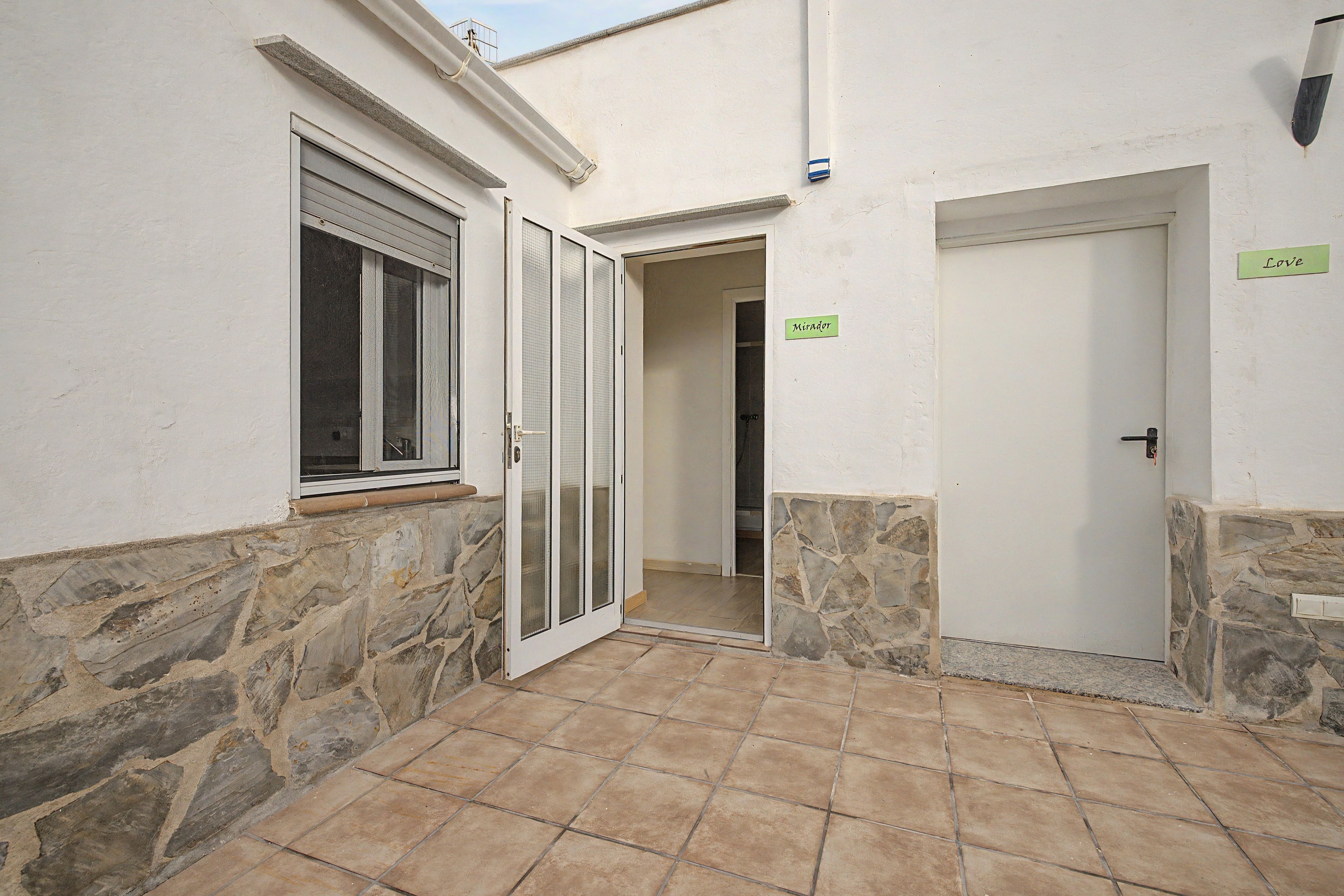 Un pasillo estrecho con una pared de piedra a un lado y una pared blanca al otro, que conduce a una puerta con un letrero que dice 'Mirador'.