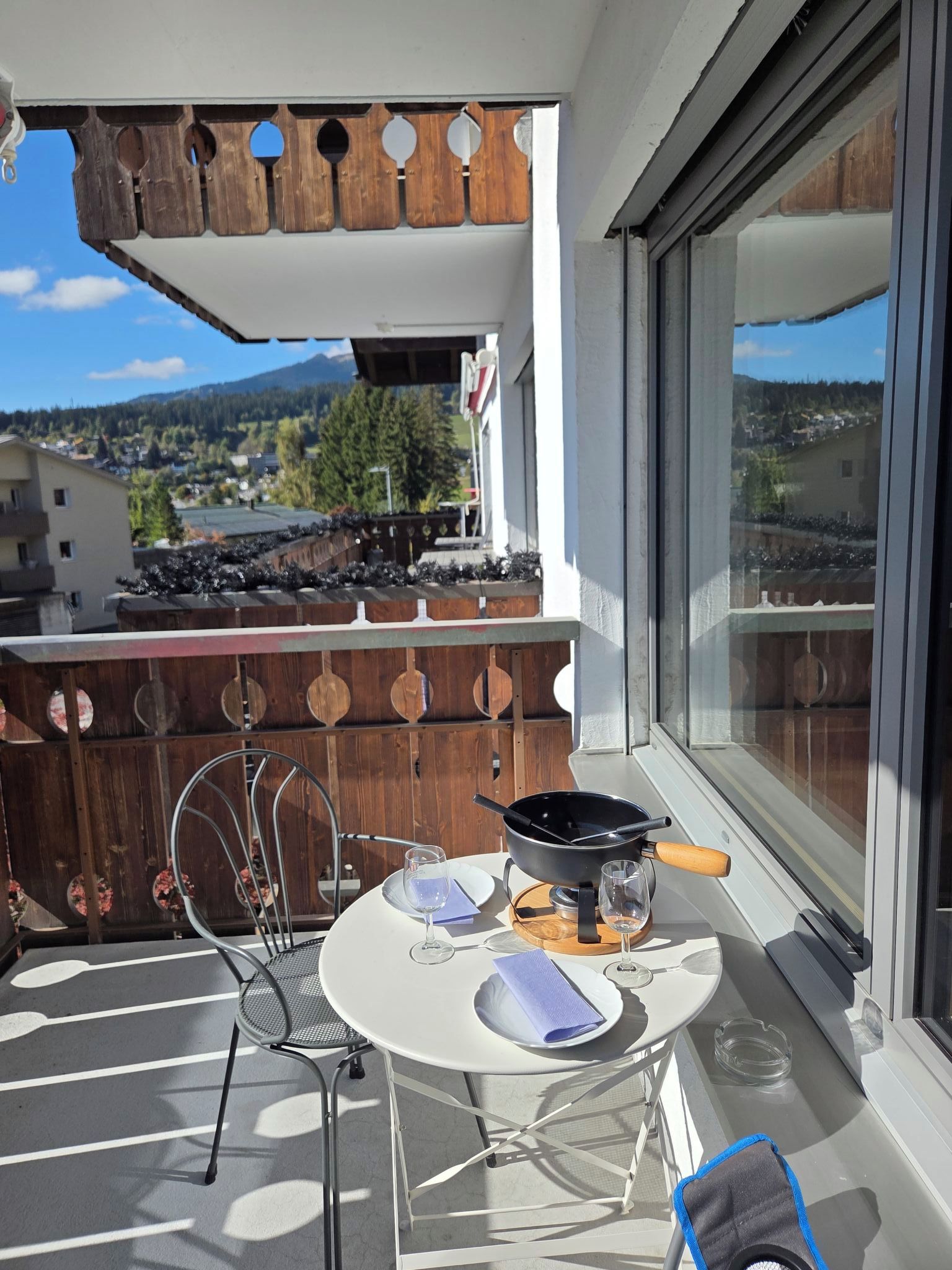 A balcony with a table set for two, a chair, and a view of a mountainous landscape.