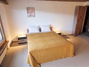 A bedroom with a large bed, two bedside tables, a nightstand, a wooden door, and a framed picture on the wall. - Piz Fess by Interhome (Flims)