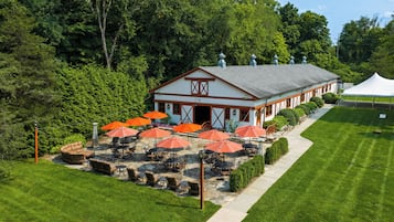 A building with a covered patio area, outdoor seating with tables and chairs, and a white tent in the background.