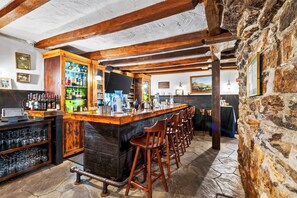 Eine Bar mit Holzbalken, einer Steinwand und einer Theke mit Hockstühlen.