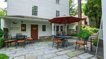 A patio area with stone flooring, outdoor seating with metal tables and chairs, and a red umbrella.