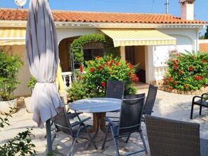 An outdoor patio with a round table and chairs, a covered umbrella, and a house with a tiled roof and potted plants. - Holiday Home in Vinaros With Swimming Pool (Vinaros)