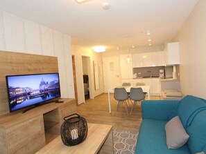 A modern living room with a flat-screen TV, a blue sofa, and a dining area with chairs. - H&P Residence Grafenmatt Type B (Feldberg)