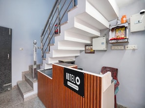 Ein Hotel-Rezeptionstresen mit einem Schild, das eine betriebliche Abwicklung anzeigt, eine Treppe mit Metallgeländer und ein an der Wand befestigtes Regal mit einem gerahmten Bild und einer kleinen Statue.