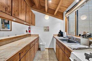 A kitchen with wooden cabinets, a sink, a stove, and a window. - Pine Views • Shared Pool + Spa | Steps to Northstar Shuttle | Northstar Pines (Truckee)