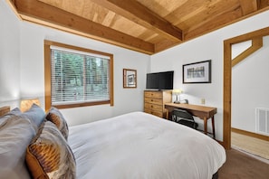 A bedroom with a bed, a desk, a chair, a television, and a window with blinds. - Pine Views • Shared Pool + Spa | Steps to Northstar Shuttle | Northstar Pines (Truckee)