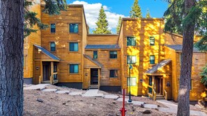 A modern multi-story building with a wooden facade, multiple windows, and a fire hydrant in the foreground. - Pine Views • Shared Pool + Spa | Steps to Northstar Shuttle | Northstar Pines (Truckee)