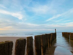 A coastal scene with wooden posts extending into the water, a sandy beach, and a clear sky. - Holiday Home With 1 Bedroom (Aagtekerke)