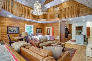 A cozy cabin interior with a wooden ceiling, a leather sofa, a dining table, and a kitchen area. - Brevard Retreat w/ Hot Tub & Copper Soaking Tub (Brevard)